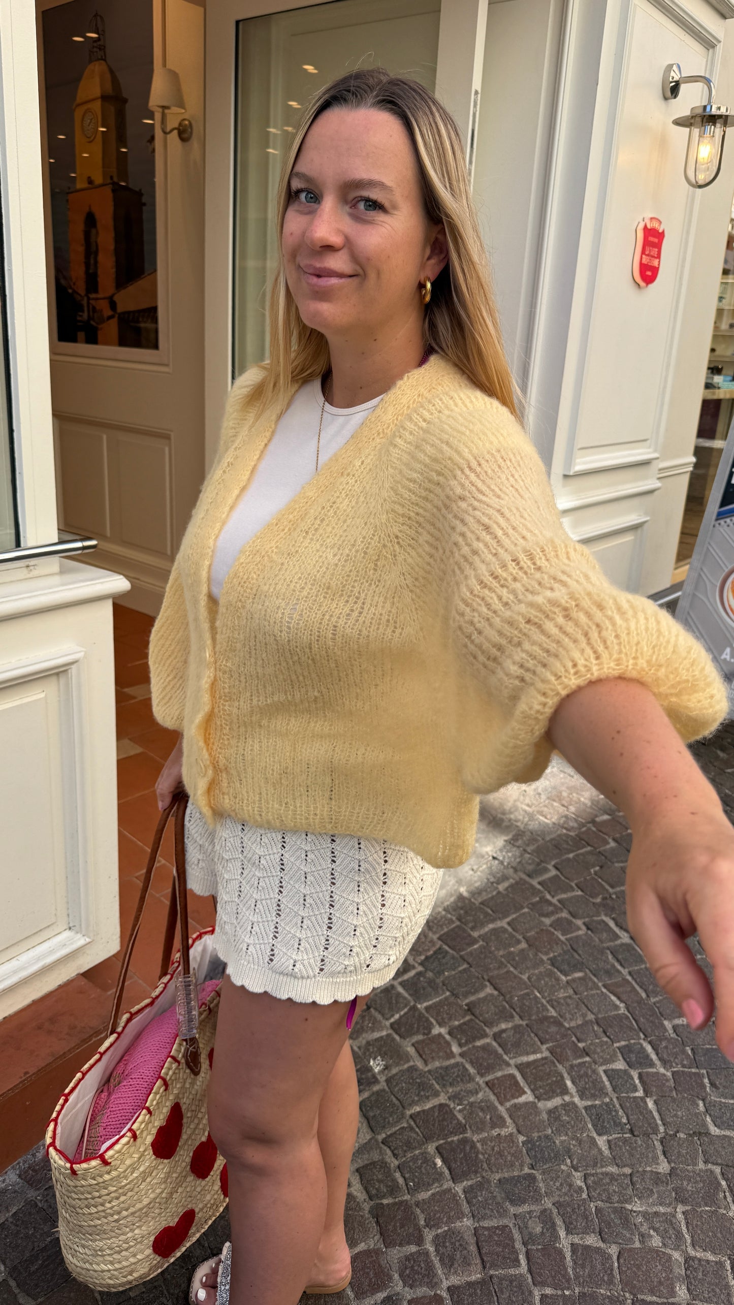 Hand knitted mohair cardigan in butter yellow worn in a French Riviera inspired street scene.