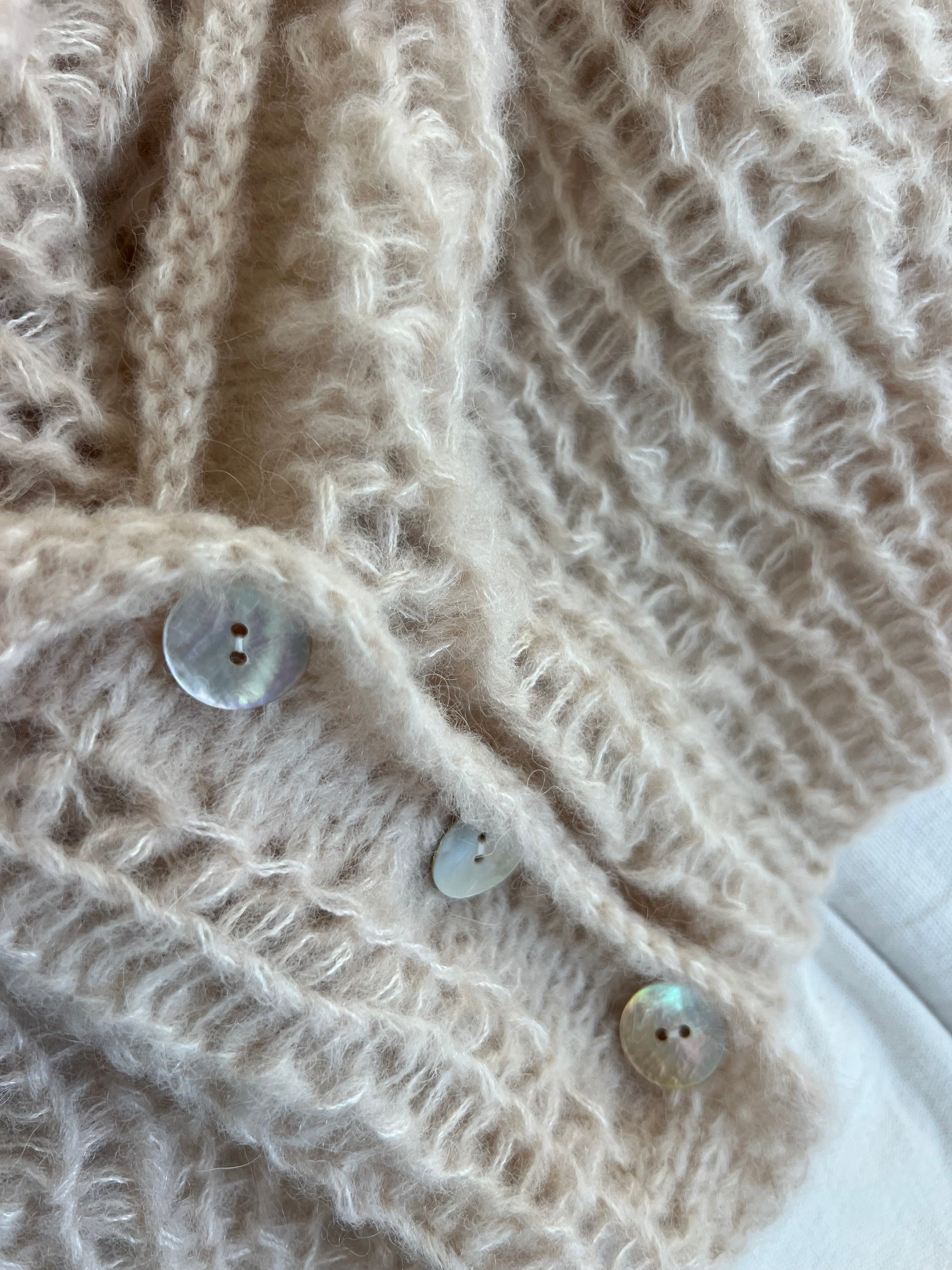 Close up of a hand knitted alpaca silk cardigan in half fisherman rib with mother of pearl buttons, soft fluffy texture and delicate stitch definition